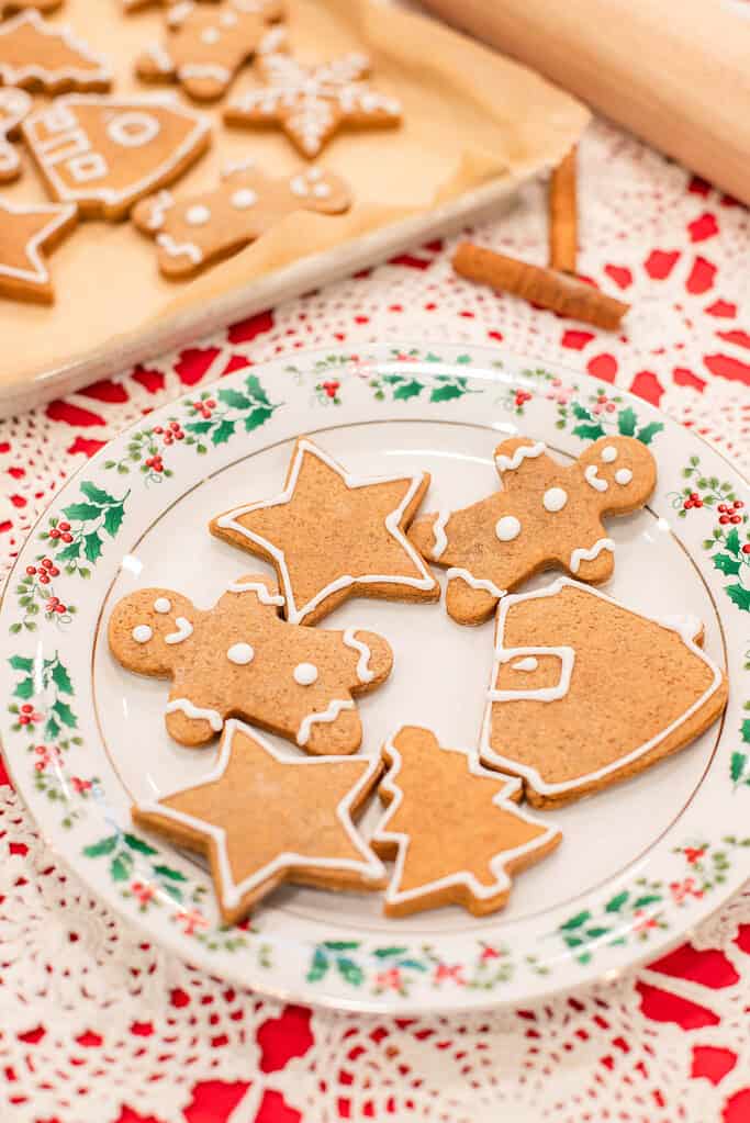 A close shot of the holly plate filled with gingerbread cookies in different holiday shapes. The texture of the cookies shows soft crumb and smooth edges, and the white icing outlines add a simple, classic finish.