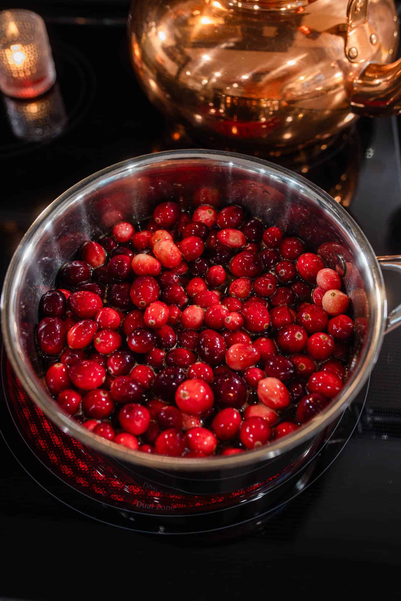 Fresh cranberries simmering in a saucepan on the stovetop as they begin to soften and release their juices.