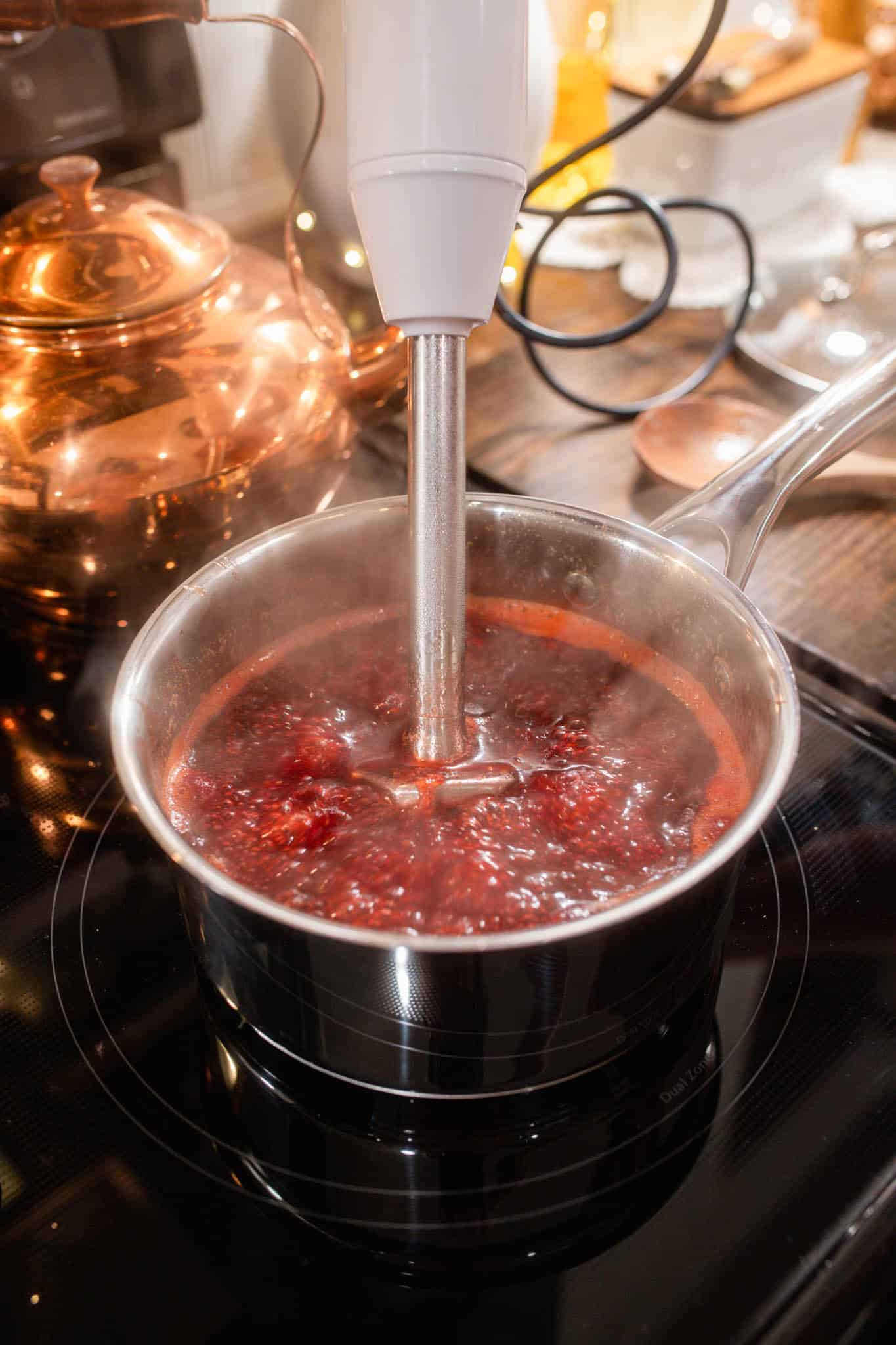An immersion blender blending hot cooked cranberries in a saucepan to make a smooth cranberry orange sauce.
