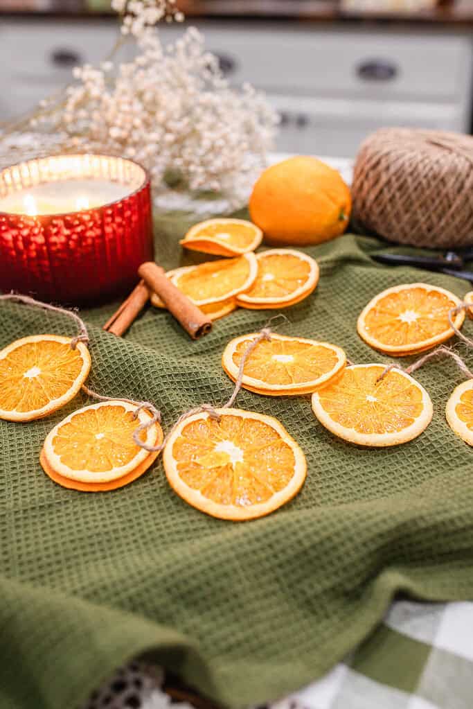 Close-up view of dried orange slices threaded with twine into a garland resting on a green cloth with soft kitchen background details.