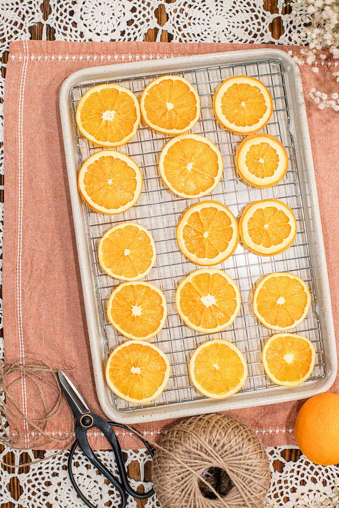 Fresh orange slices arranged in rows on a wire baking rack set over a sheet pan, preparing oranges to be dried for a homemade garland.