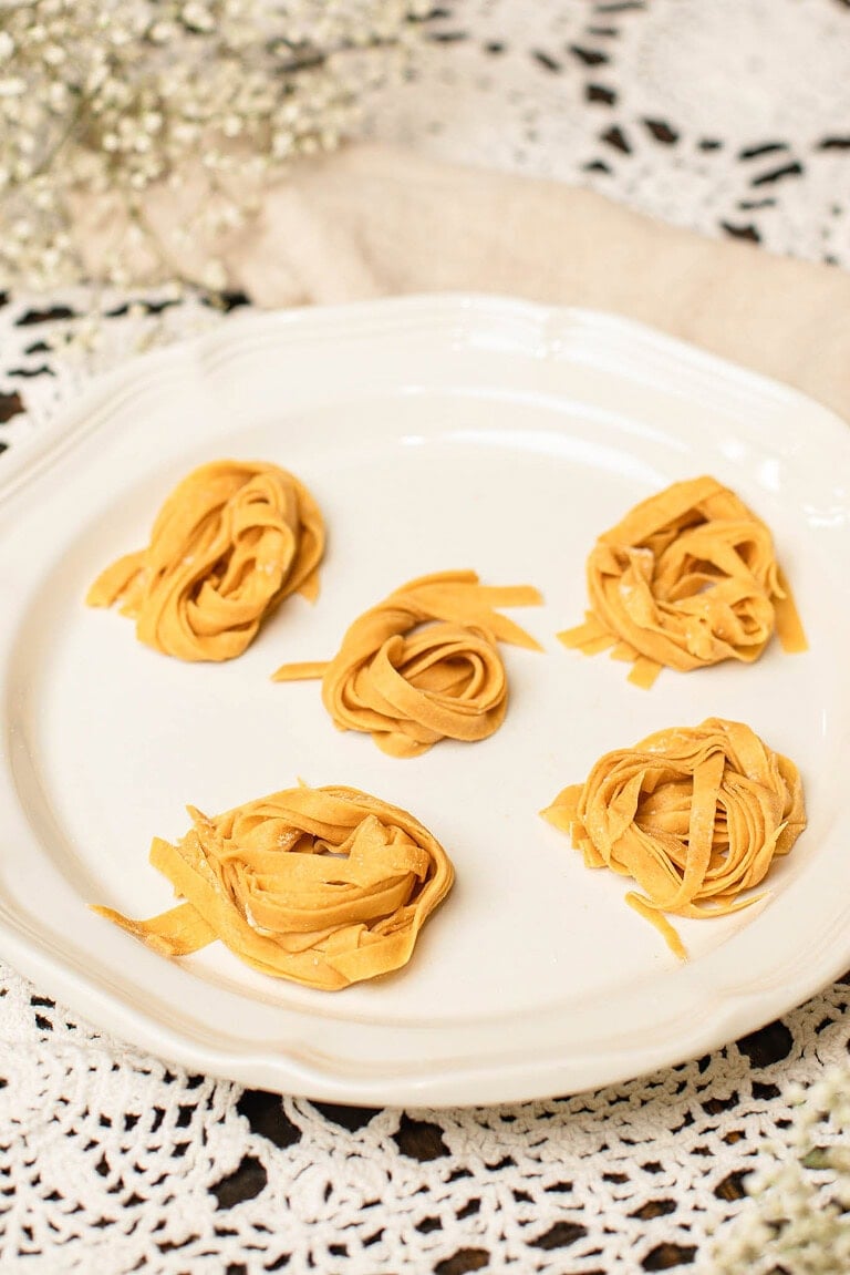 Sourdough einkorn pasta nests arranged on a white plate over a lace tablecloth.