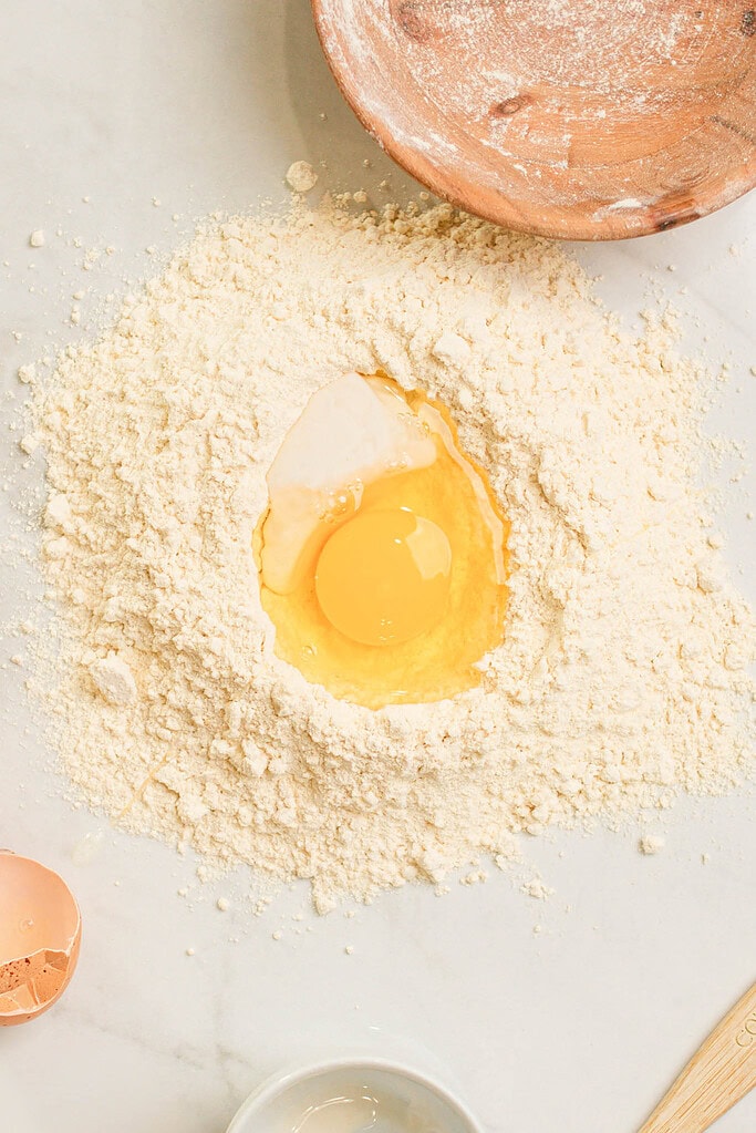 Egg and sourdough starter in a well of einkorn flour on a marble surface, ready to mix for pasta dough.