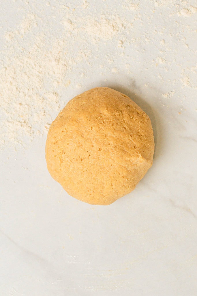 Smooth ball of sourdough einkorn pasta dough resting on a lightly floured surface.