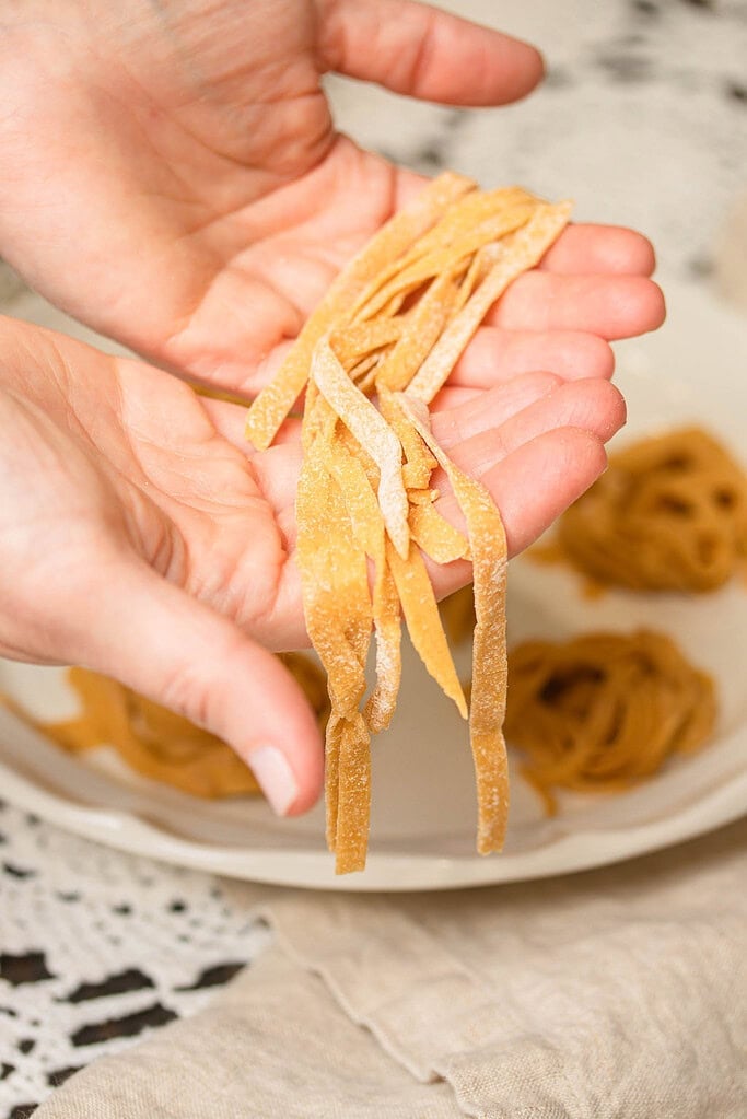 Hand holding fresh-cut sourdough einkorn pasta strands dusted lightly with flour.