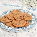 A blue and white floral plate piled with brown butter chocolate chip cookies made with freshly milled flour on a white eyelet tablecloth with baby's breath flowers and sage green cabinets in the background