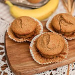 Banana muffins with freshly milled flour cooling on a wood board next to a ripe banana and muffin tin
