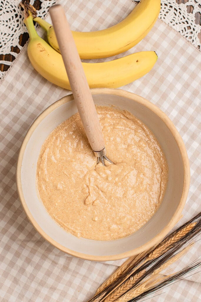 Banana muffin batter made with freshly milled flour, ripe bananas, and wheat stalks in the background