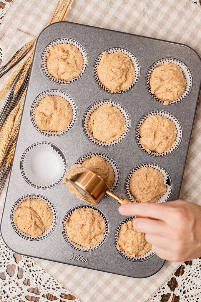 Scooping banana muffin batter into a lined muffin tin using a cookie scoop