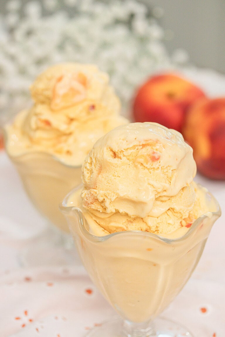 Brown butter peach custard ice cream scoops in glass dishes with fresh peaches in the background