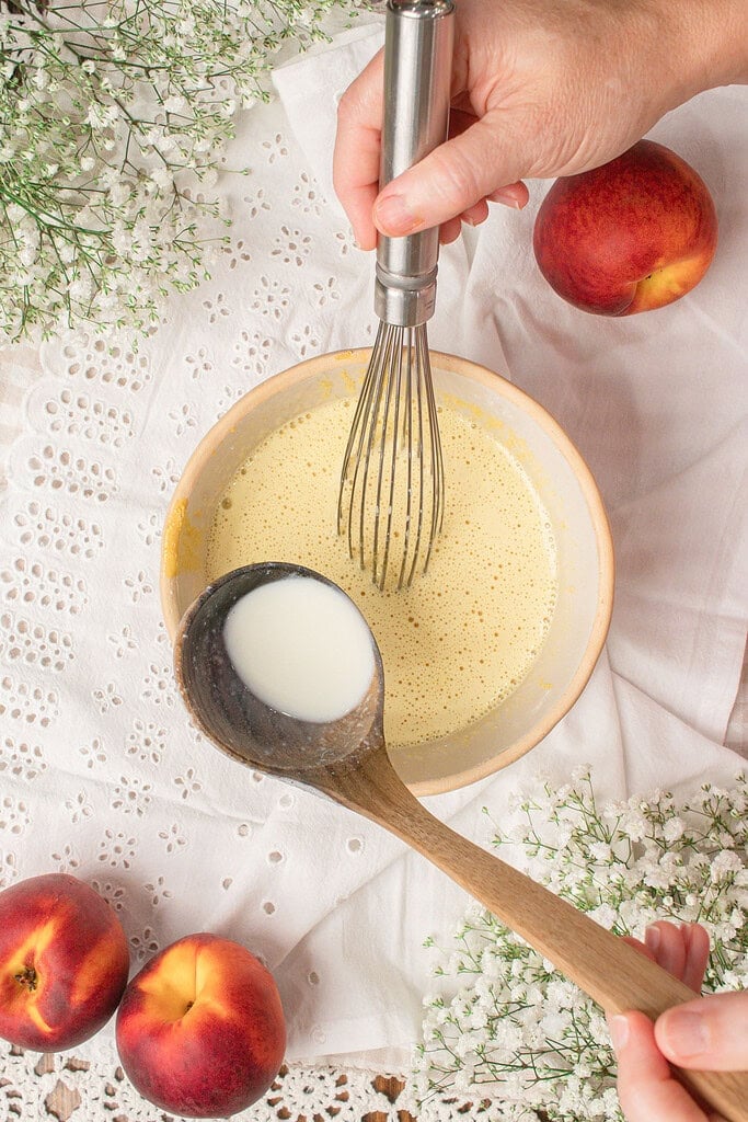 Whisking egg yolks and brown butter with a splash of cream being added from a wooden spoon