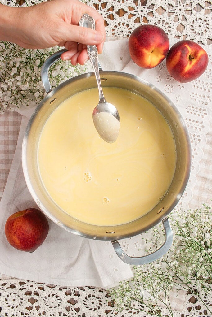 Tempering custard base with a spoon over a saucepan of warm cream mixture