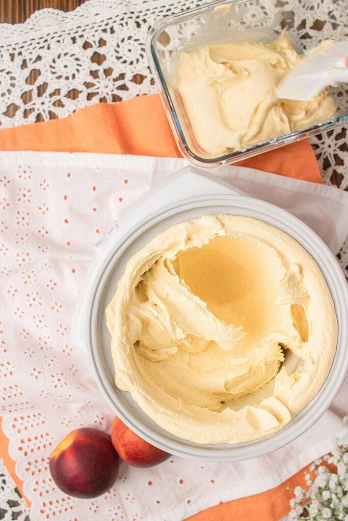 Churned brown butter peach custard ice cream in an ice cream maker next to a container of soft serve