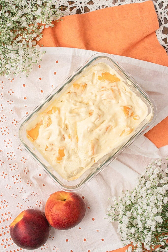 Overhead view of brown butter peach custard ice cream with peach chunks in a glass storage container