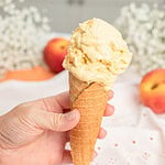 Hand holding a waffle cone topped with a scoop of brown butter peach custard ice cream