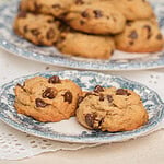 Brown butter sourdough chocolate chip cookies on a blue and white floral plate with a full plate of cookies and fresh flowers in the background