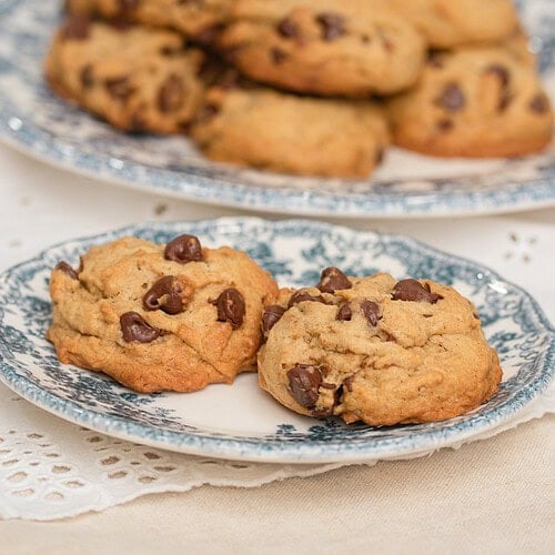Brown butter sourdough chocolate chip cookies on a blue and white floral plate with a full plate of cookies and fresh flowers in the background