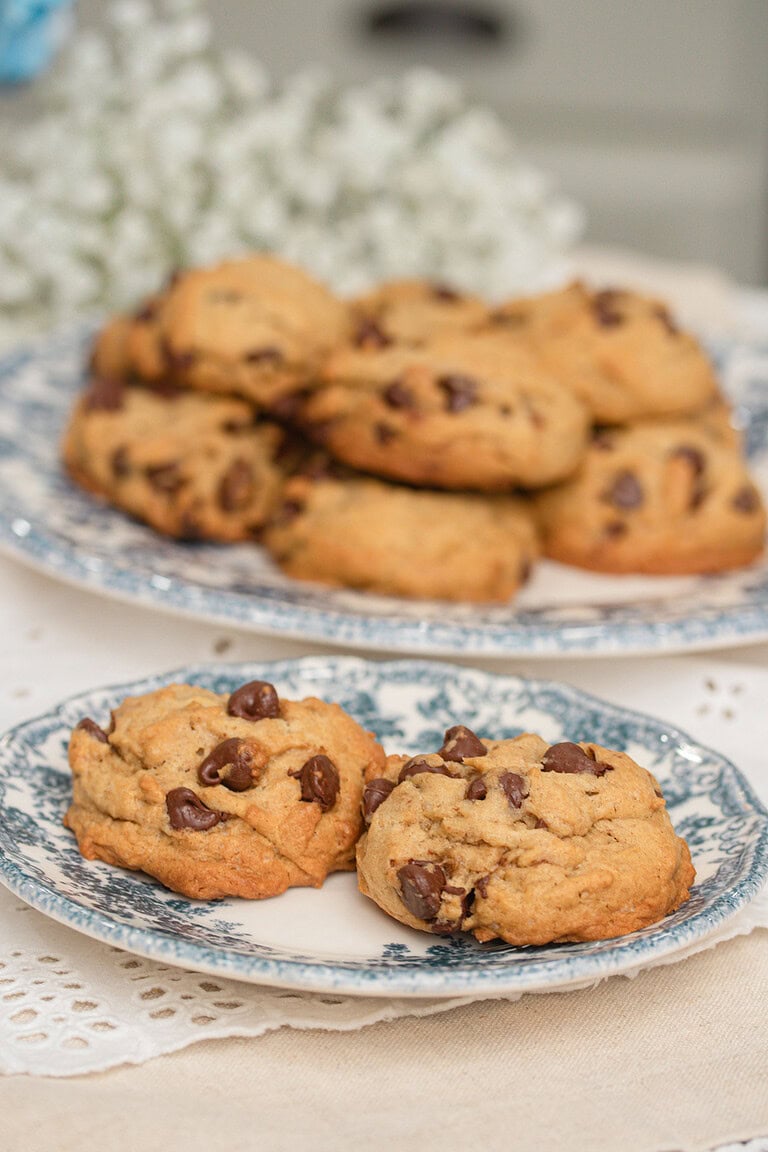 Brown butter sourdough chocolate chip cookies on a blue and white floral plate with a full plate of cookies and fresh flowers in the background