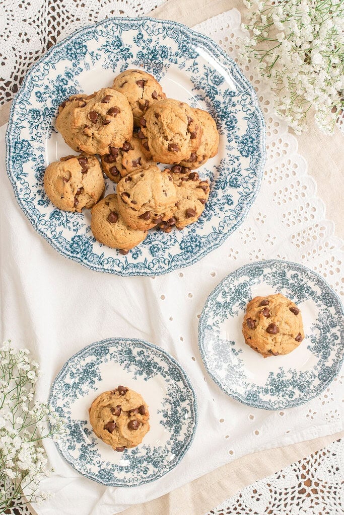 Overhead view of brown butter sourdough chocolate chip cookies arranged on vintage blue and white floral plates surrounded by baby's breath flowers