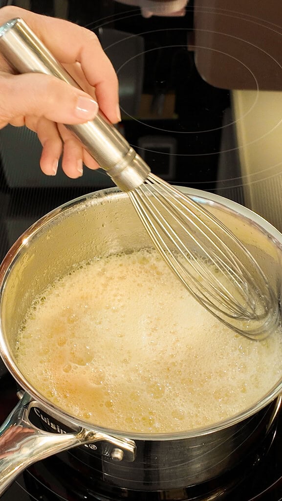 Butter being whisked in a saucepan on the stovetop as it browns into a golden foamy brown butter for sourdough chocolate chip cookies