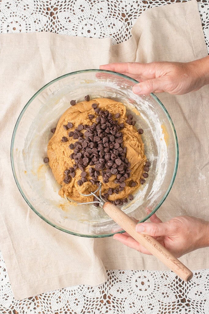 Mini chocolate chips being folded into finished brown butter sourdough cookie dough with a wooden spoon