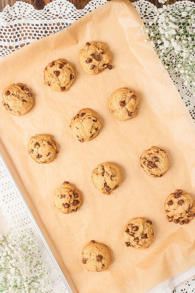 Freshly baked brown butter sourdough chocolate chip cookies cooling on a parchment-lined baking sheet surrounded by baby's breath flowers