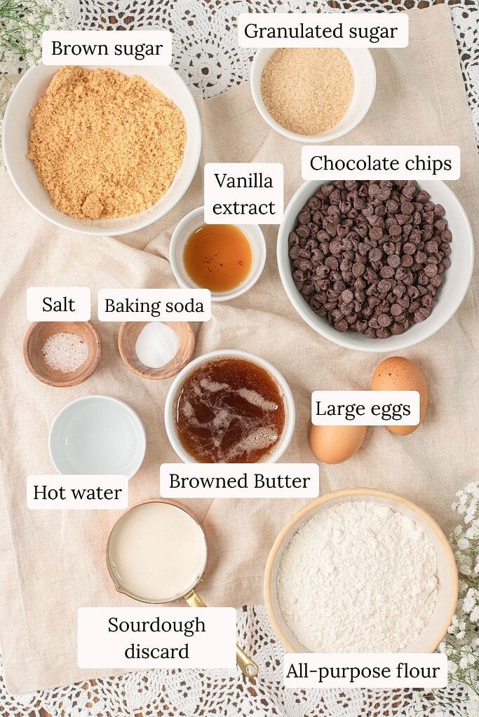 Ingredients for brown butter sourdough chocolate chip cookies including brown sugar, granulated sugar, chocolate chips, vanilla extract, salt, baking soda, browned butter, hot water, large eggs, sourdough discard, and all-purpose flour