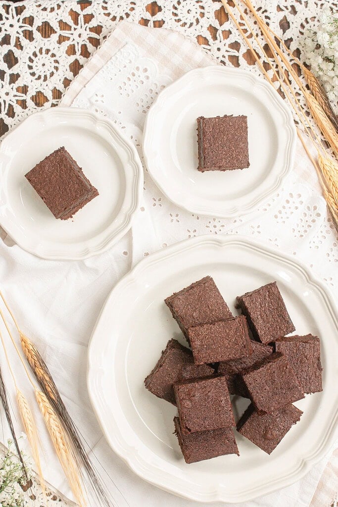 Cakey brownies made with freshly milled flour cut into squares and arranged on vintage white plates surrounded by dried wheat stalks and baby's breath
