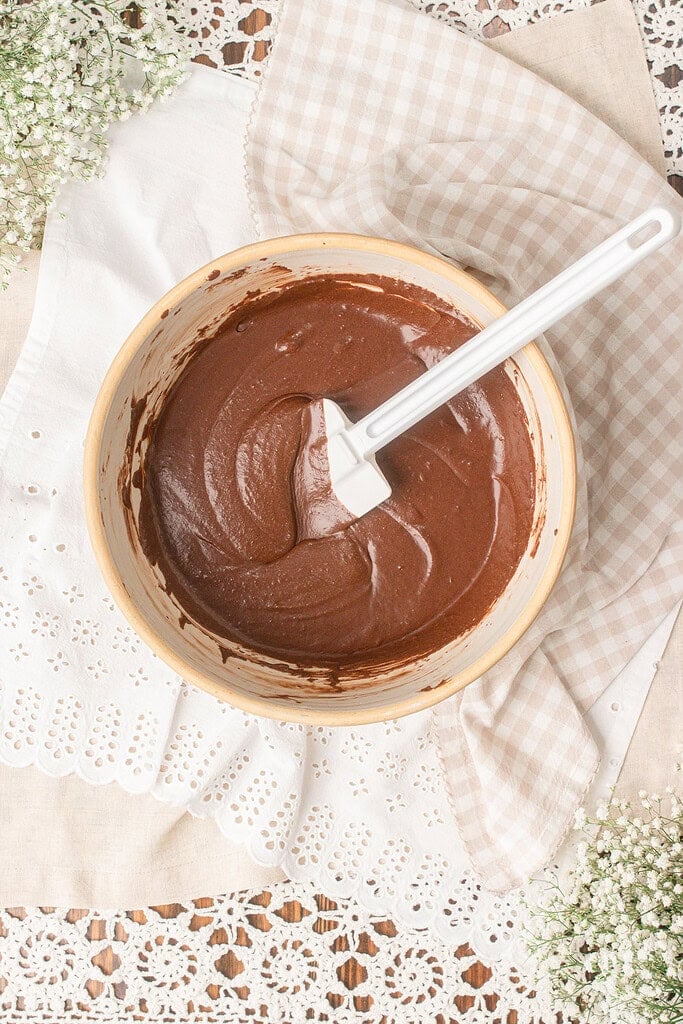 Freshly milled flour brownie batter being mixed in a bowl with a white spatula showing a smooth glossy chocolate texture