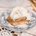 A cinnamon roll made with freshly milled flour topped with cream cheese frosting on a vintage floral plate