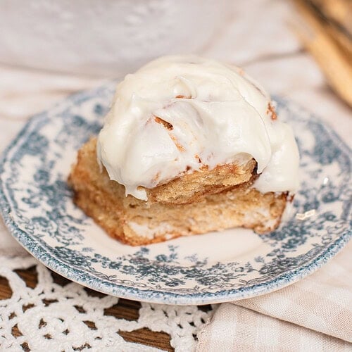 A cinnamon roll made with freshly milled flour topped with cream cheese frosting on a vintage floral plate