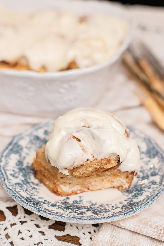 A cinnamon roll made with freshly milled flour topped with cream cheese frosting on a vintage floral plate