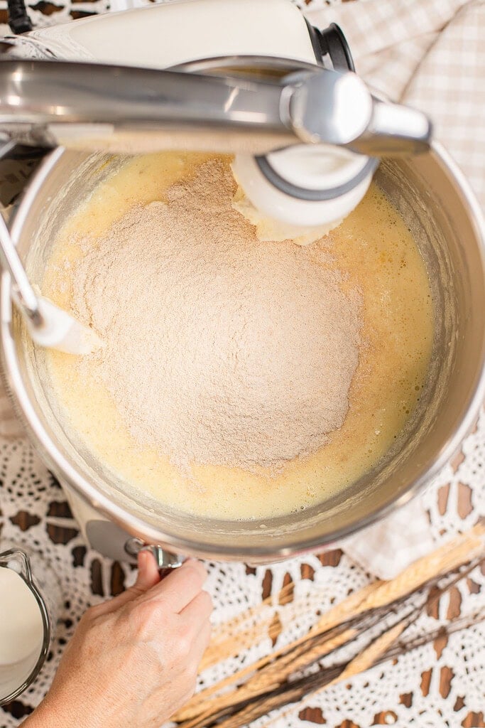 Adding freshly milled flour to the wet dough ingredients in a stand mixer for cinnamon rolls