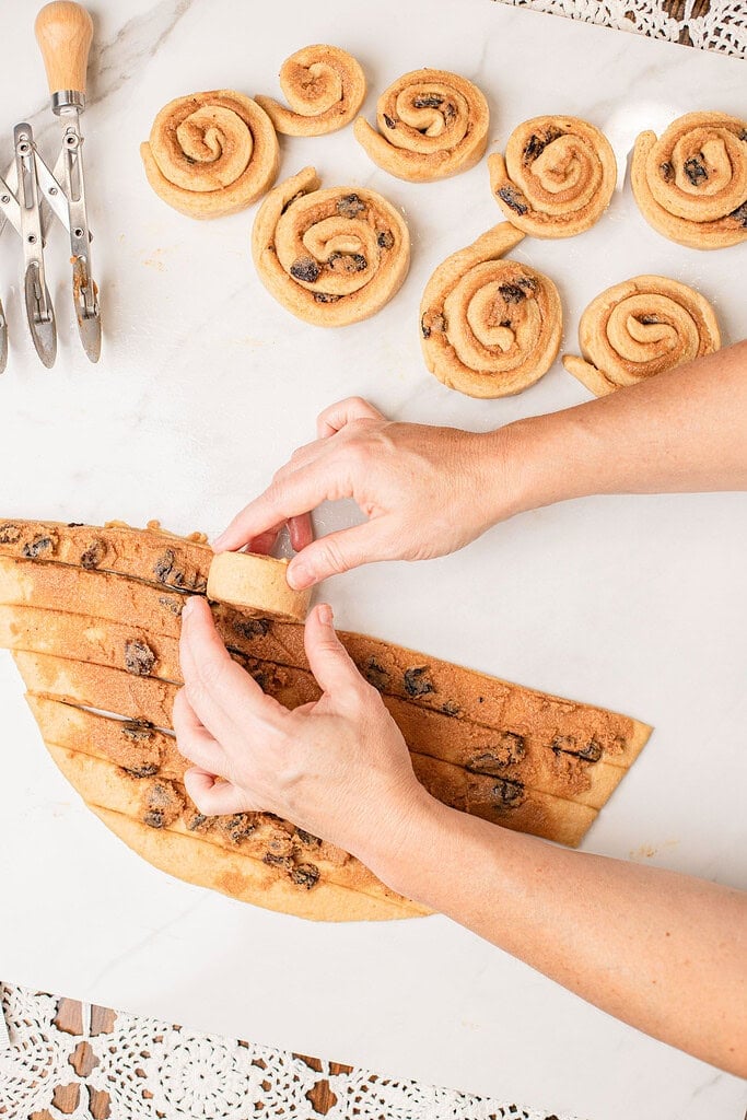 Slicing rolled cinnamon dough into individual rolls before the second rise