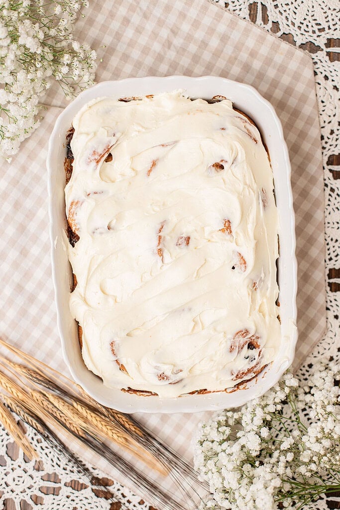 Cinnamon rolls made with freshly milled flour covered in cream cheese frosting in a baking dish