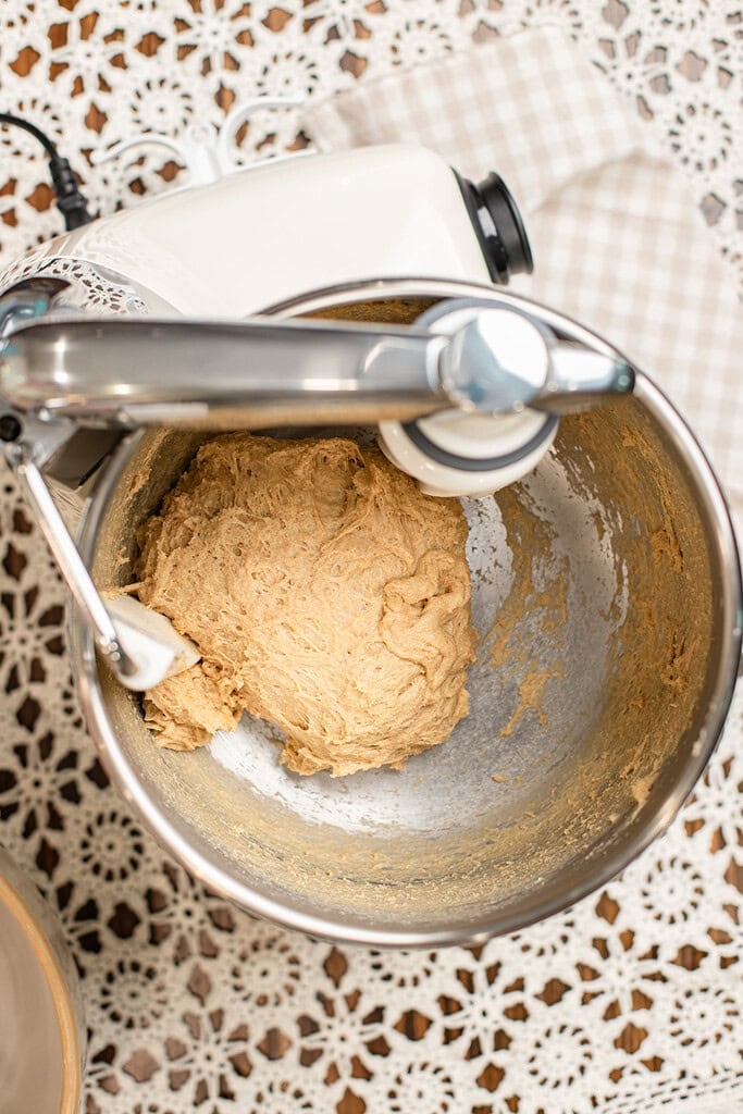 Overhead view of smooth, stretchy dinner roll dough made with freshly milled flour in a stand mixer bowl after kneading, showing developed gluten strands.
