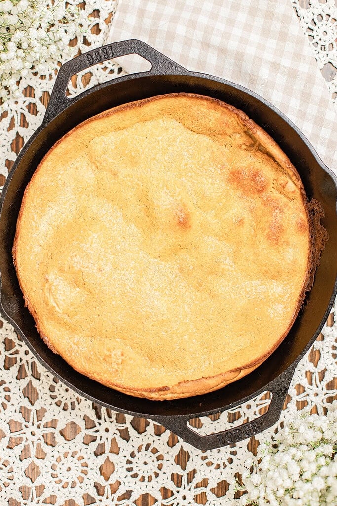 Overhead view of a fully puffed whole wheat Dutch baby pancake baked golden brown in a cast iron skillet, with dramatic risen edges and a lightly browned surface.