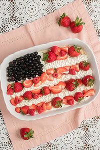 Finished Fruit Pizza with Freshly Milled Flour decorated as a flag design with blueberries, piped whipped cream, sliced strawberries, and raspberries, resting on pink linen with loose strawberries scattered around