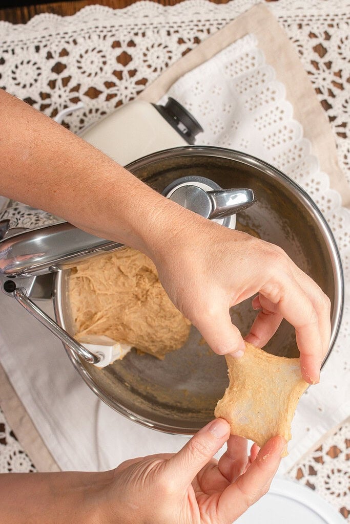 Hands performing a windowpane test on a stretched piece of dough to check gluten development for hamburger buns