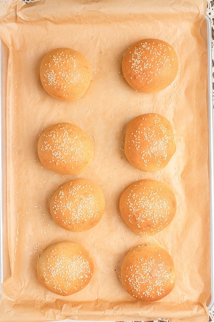 Baked Fresh Milled Flour Hamburger Buns topped with sesame seeds cooling in even rows on a parchment lined baking sheet