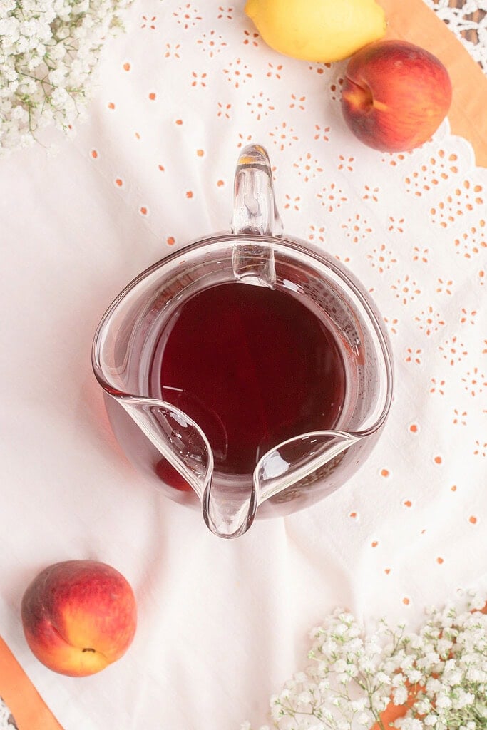 Freshly brewed black tea for homemade peach iced tea cooling in a clear glass pitcher before adding peach syrup and ice.