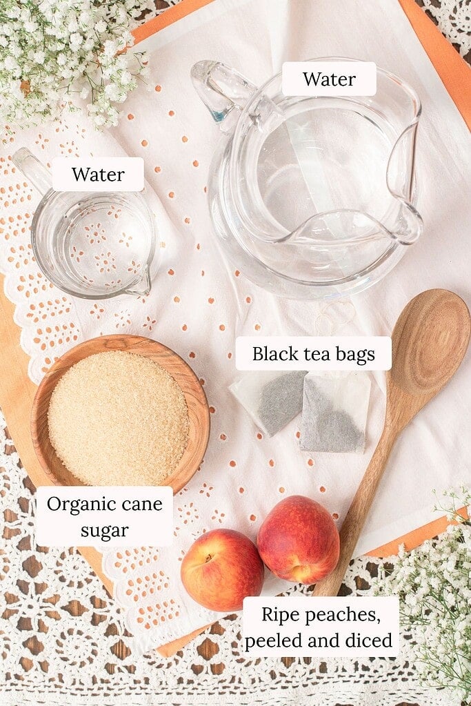 Ingredients for homemade peach iced tea including ripe peaches, black tea bags, organic cane sugar, and water arranged in a bright overhead flat lay with a wooden spoon.