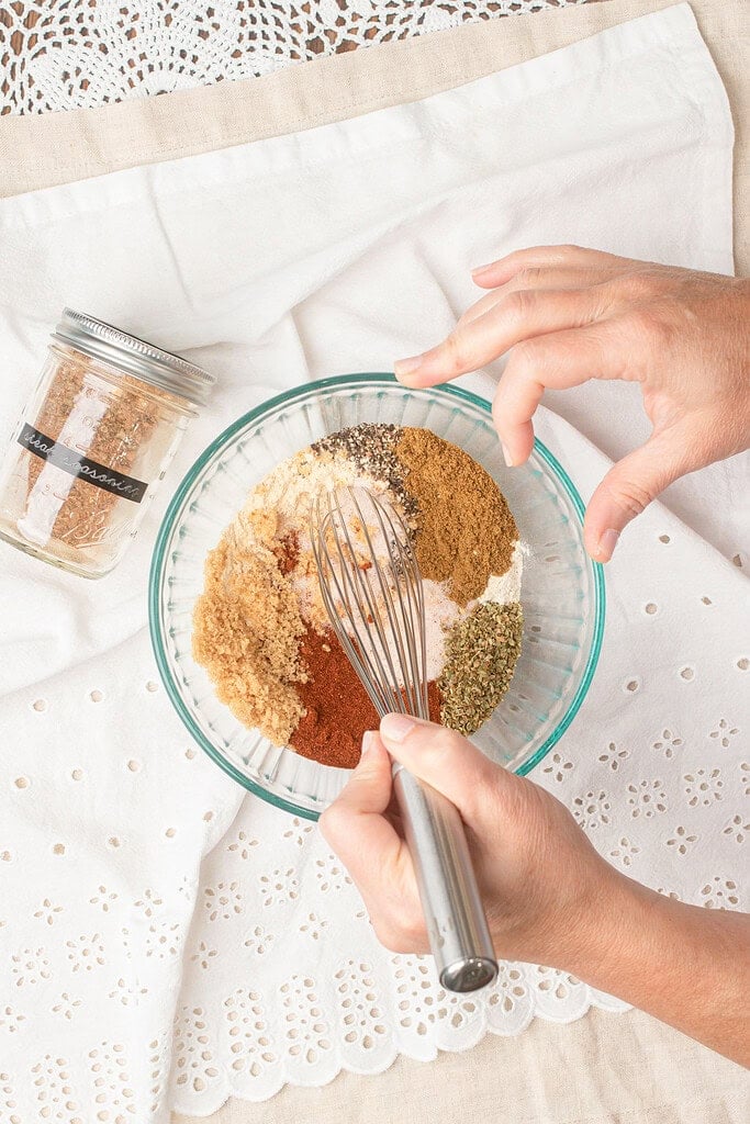 Hands whisking together smoked paprika, brown sugar, garlic powder, and other spices to make homemade steak seasoning