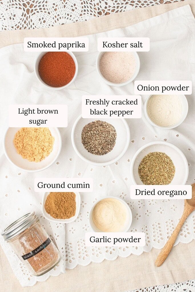Ingredients for homemade steak seasoning including smoked paprika, kosher salt, onion powder, freshly cracked black pepper, dried oregano, ground cumin, garlic powder, and light brown sugar in small bowls