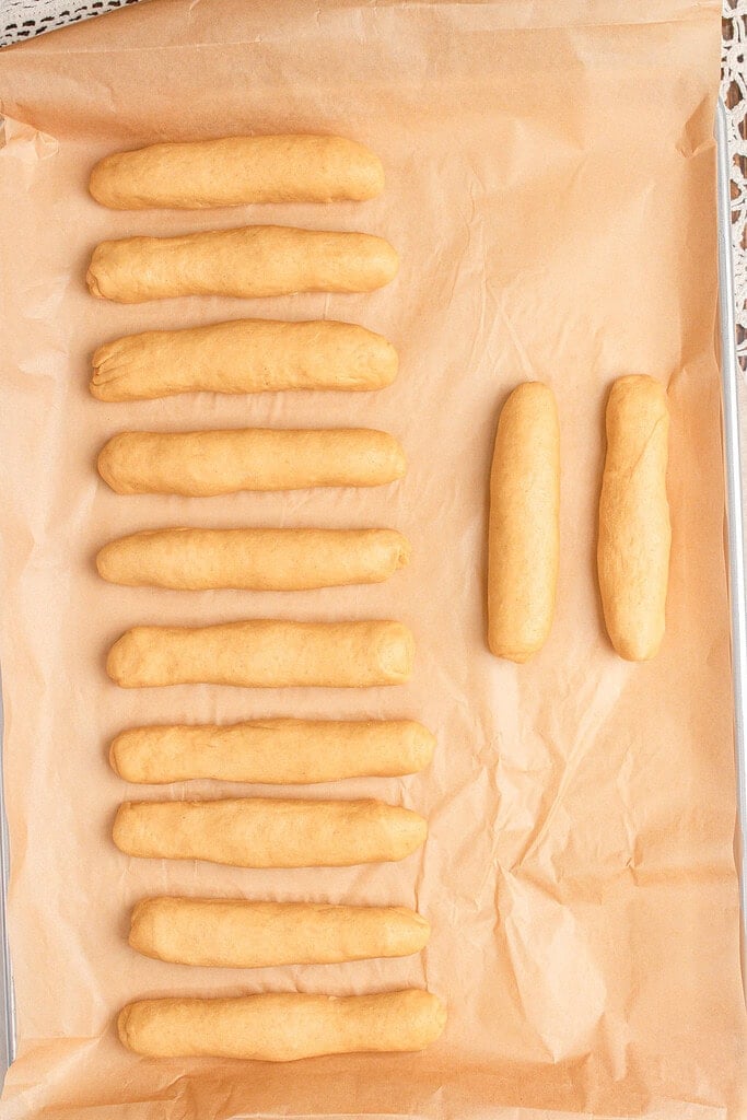 Shaped unbaked hot dog buns made with freshly milled flour lined up in rows on a parchment-lined baking sheet ready to rise
