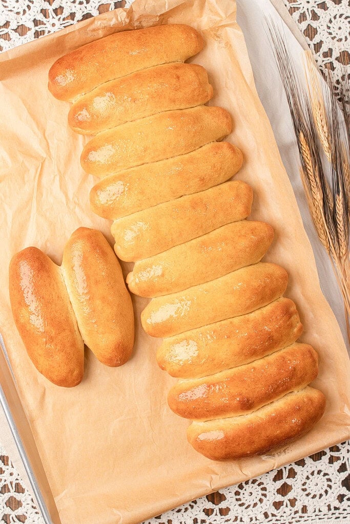 Freshly baked hot dog buns made with freshly milled flour arranged in rows on a parchment-lined baking sheet with a golden glossy crust