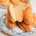 A split hot dog bun made with freshly milled flour showing its soft fluffy crumb, stacked with more buns on a blue and white floral plate
