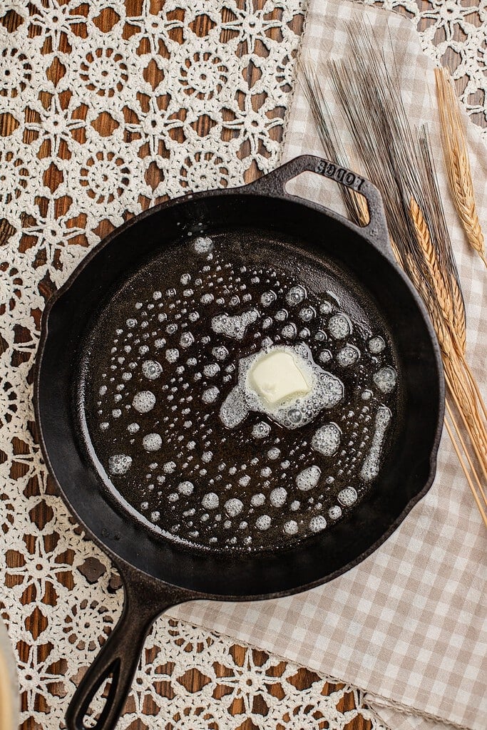 Overhead view of butter melting and bubbling in a hot cast iron skillet, ready for cooking pancakes made with freshly milled flour.