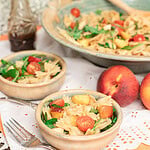 Peach caprese pasta salad served in small bowls with fresh peaches and a serving bowl in the background