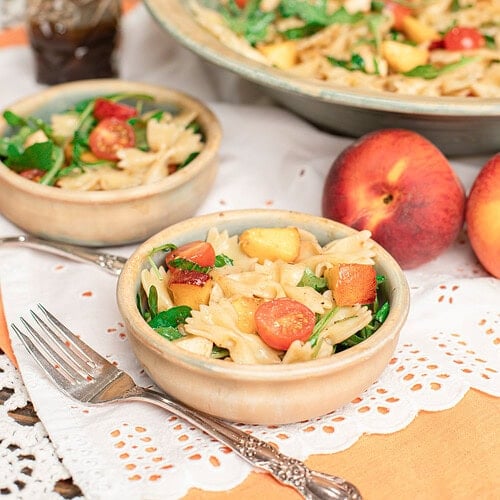 Peach caprese pasta salad served in small bowls with fresh peaches and a serving bowl in the background